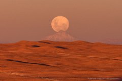 The full moon is rising just above the distant Llullaillaco volcano. View from Paranal Observatory, Chile