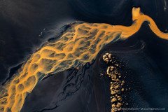 Aerial photo of yellow water flowing over black lava sand, creating abstract art, Iceland