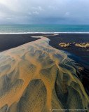 Aerial photo of yellow glacial river flowing over black lava sand, creating abstract art, Iceland