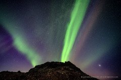 Northern Lights seems to send light beams out of a small volcano crater, Iceland