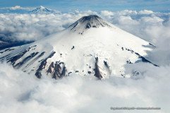 Aerial photo of Snow covered volcano Villarrica above a cloud layer, Lanin in the background